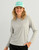 HUK Pursuit Graphic - Huk Circle Palm, a woman wearing a light gray long sleeve athletic shirt with HUK logo and a teal and white cap with HUK emblem, smiling against a plain white background.