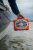 TURTLEBOX Audio Gen3 Speaker, rugged portable waterproof speaker being held over water near a boat.