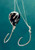 Hook'd On Reelin' Black Ice, close-up of a black and white fishing jig with two treble hooks and a black bead, blue background.