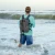 TSUNAMI Tsunami Saltx Waterproof Backpack, a person wearing a gray waterproof backpack while standing in the ocean waves.