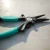 TOADFISH Toadfish Inshore 8" Stainless Pliers - Elite Series, close-up of the black and teal fishing pliers lying on a textured surface.