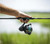 TOADFISH Toadfish Carbon II Spinning Combos, a person holding a fishing rod with a spinning reel in an outdoor setting by the water.