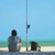 TOADFISH Toadfish Surf Combo, image of a person sitting on the beach with a fishing rod and gear on the sand, overlooking the ocean.