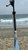 DEERFIELD FABRICATION Deerfield Open Face 2.0 Sand Spike, a metal fishing spike standing on the sandy beach with the ocean and cloudy sky in the background.