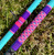 Nick's Custom Rods 2026, colorful fishing rods with vibrant pink, purple, and blue geometric patterns laying on grass.