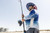 QUANTUM Quantum Merit Spinning Reel, a man fishing with a spinning reel and rod on a beach wearing patriotic-themed hat and sunglasses.
