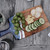 Toadfish Wooden Coastal Serving Board, a wooden serving board with slices of cucumber, cheese, bread, and green grapes on it.