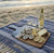 Toadfish Wooden Coastal Serving Board, a wooden platter with oysters, cheese, crackers, lemon slices, and a dipping sauce, set on a blue striped beach towel on the sand with a bottle of white wine and two glasses at the beach during sunset.