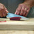 TOADFISH Toadfish 8" Abalone Chef Knife, person slicing a piece of tuna fish on a wooden cutting board with a blue and white ceramic knife.