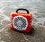 TURTLEBOX Turtlebox Cub, portable waterproof speaker with a red rugged exterior and a white speaker grille, placed in shallow water