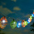 Solar string lights for patio have 20 Blue-Orange-Purple Curvet designed toppers that surround one hanging LED bulb.