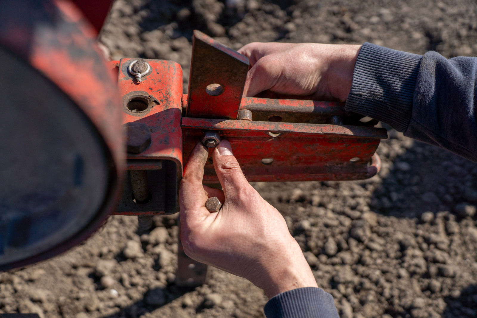 A man fastens an adjustable metal bracket with a bolt on a tractor frame