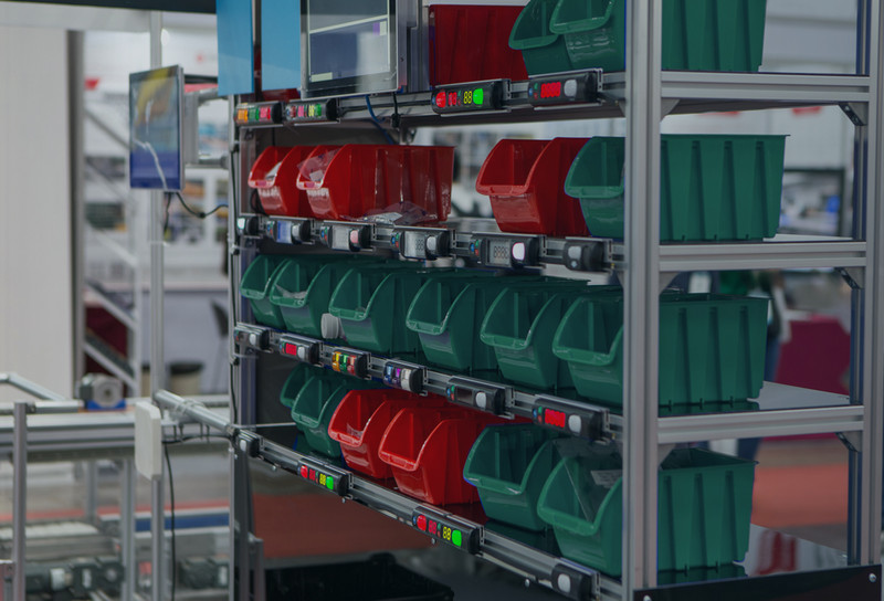 Parts in red and green bins on shelfs in a factory near workstation