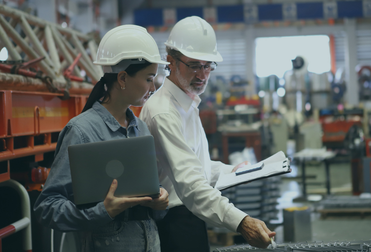 Two people in a factory with computer and papers reviewing products