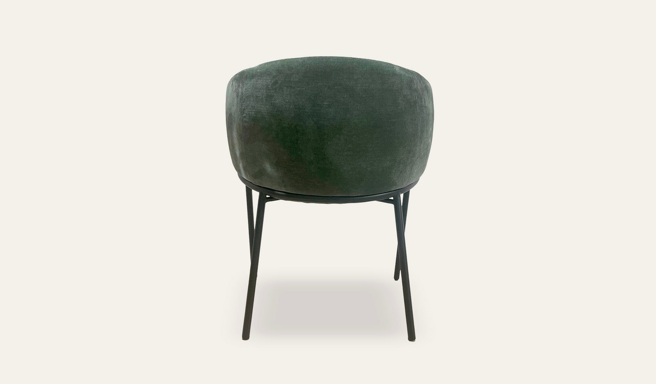 Mila dining chair with soft upholstery, curved wraparound backrest and slim black metal legs, designed for modern dining spaces.