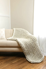 Cloud knit weighted blanket in white, draped over the corner of a cream colored couch.