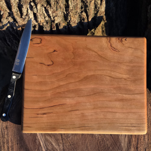 Small cherry cutting board by Treeboard with knife and walnut log. Elegant chopping board with a white background. The black cherry is a "gummy" or "heavy gum" cherry.