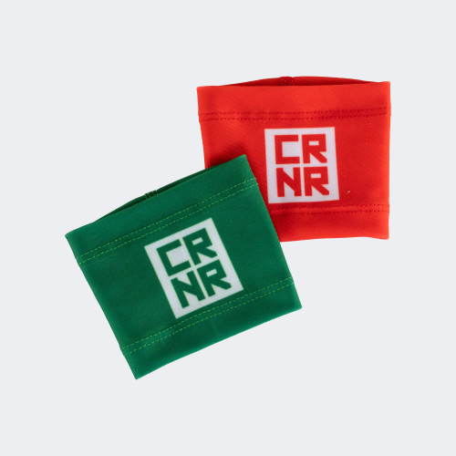 A product shot of the Combat Corner Lightweight Sublimated Scoring Wristbands, featuring one solid green wristband overlapping a solid red wristband, both displaying a white square CRNR logo on a light gray background.