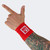 A model's tattooed arm pointing upward while wearing a red Combat Corner Lightweight Sublimated Scoring Wristband, isolated on a light gray background.