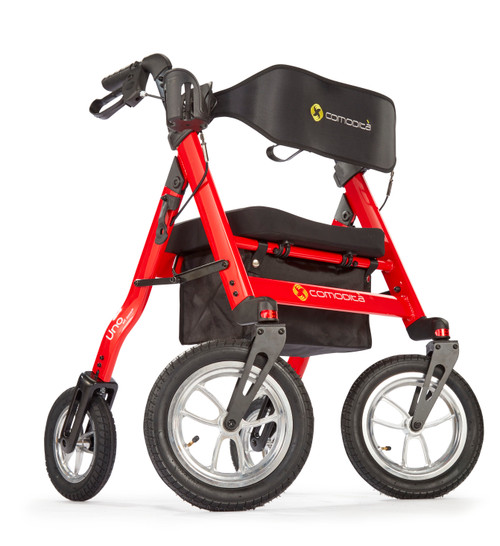 Studio shot of the Comodita Uno All-Terrain Rollator featuring a bright metallic red aluminum frame. The walker has four pneumatic tires with silver spokes; the two front wheels are larger (12 inches) than the two rear wheels (10 inches). It includes a black padded nylon seat, a black under-seat storage bag with a quilted texture, and a wide backrest strap displaying the 'Comodita' logo in yellow and white. The ergonomic handgrips are equipped with brake levers, and the overall design appears robust and modern against a plain white background.