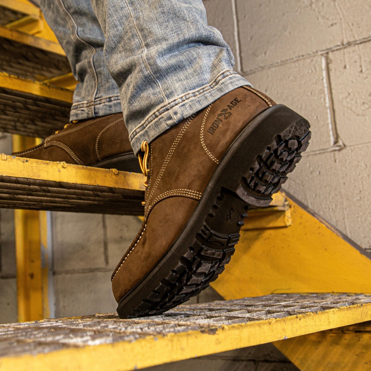 A person wearing Iron Age assembler work boots stands on metal steps in a factory.
