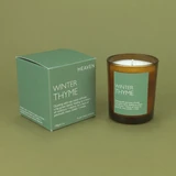 Heaven Scent Winter Thyme Christmas festive vegan natural soy and plant wax scented candle in a brown glass jar displayed beside its matching herb green presentation box against a green botanical background