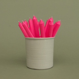 A pack of 16 bulk 10-inch UK-made straight dinner candles in bubblegum pink, arranged in a neutral cream stoneware pot against a soft olive green background.