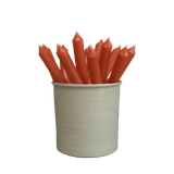 A pack of 16 bulk 10-inch UK-made straight dinner candles in burnt orange, arranged in a neutral cream stoneware pot isolated against a clean white background.