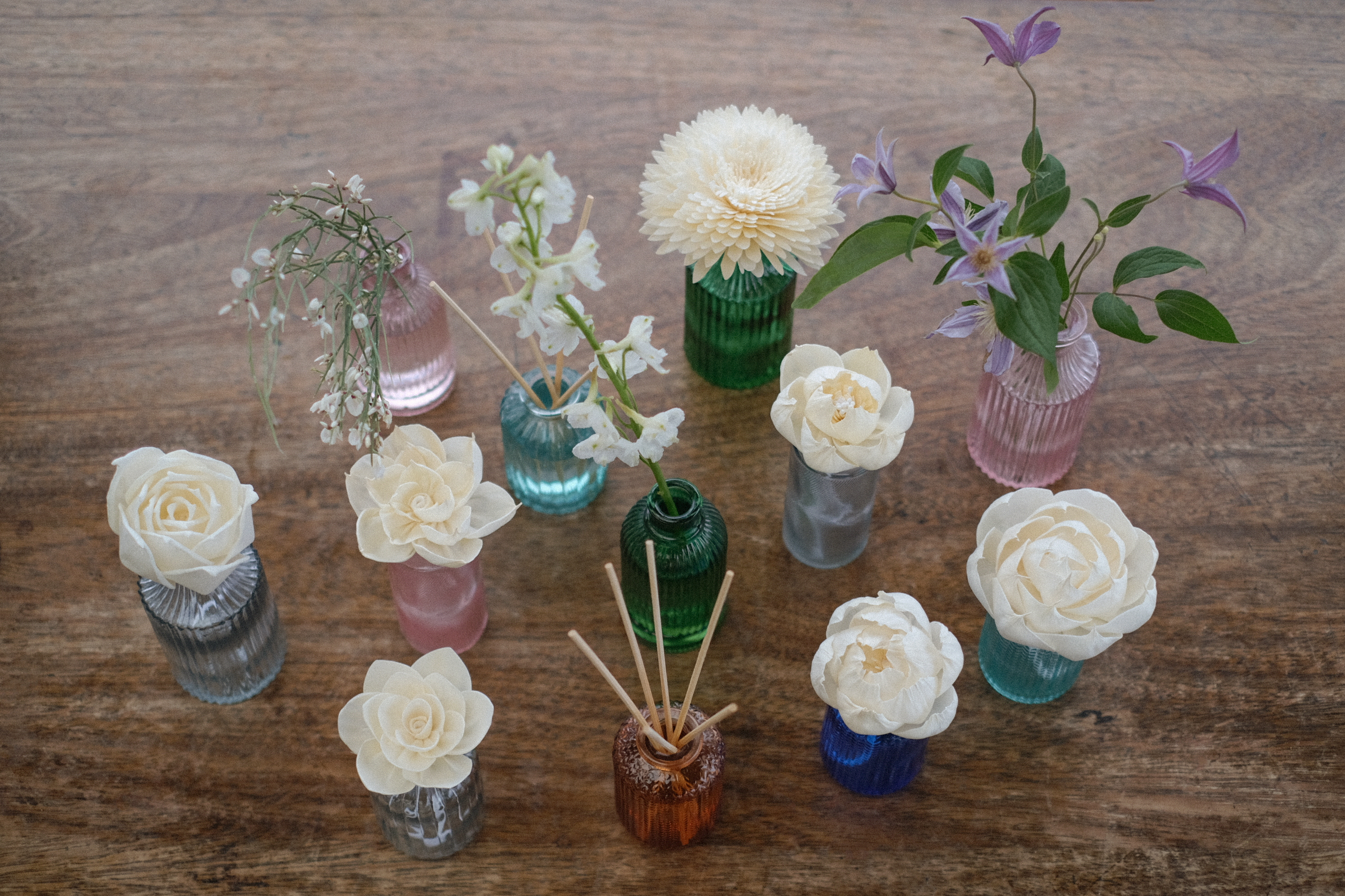 Heaven Scent Coloured bottles on a table, with reed sticks, wild flowers and sola flowers.