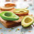 A small Avocado Hugger covers half an avocado on a wooden cutting board.