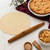 An Ironwood French rolling pin on a kitchen counter with pie dough and a baked apple pie.