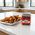 A tin of Spicewalla Carolina BBQ Rub on a kitchen island with seasoned roasted potato wedges.