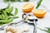 An alternate view of the RSVP Garlic Press in use surrounded by fresh garlic cloves and orange halves on a counter