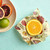 A half an orange being wrapped with the Bees Wrap Plant Based Assorted sizes 3 pack with Meadow Magic print on a table