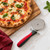 A Prep Solutions stainless steel pizza wheel sits next to a fresh-from-the-oven pizza on a wooden cutting board.