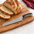 A Tovolo Comfort Grip 8.5 Inch Serrated Bread Knife on a wooden cutting board with an artisan loaf of bread.