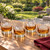 Each of the four sports ball ice shapes in a rocks glass with bourbon on a patio table with a beautiful, thoughtfully landscaped backyard in the background.