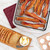 An overhead shot of the Nordic Ware Oven Crisp Baking Tray with bacon on a table next to bread, butter, and eggs.