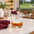 A golf ball-shaped ice cube made with the Tovolo Golf Ball Ice Molds in a rocks glass with bourbon on a kitchen island with a golf tournament on a TV in the background.