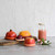 The five sizes of the Food Huggers in Terra Cotta with fruit and covering a bottle on a counter