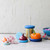 The five sizes of the Food Huggers in Ice Blue with fruit and a can on a counter