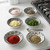 The six pinch bowls in the Now Designs black bits & dots pinch bowl set are filled with herbs and spices next to a stovetop.