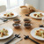 The dipping bowls in the Danica Heirloom Unite Element Dipping Bowl Set on a dining table filled with soy sauce, surrounded by 4 place settings with gyozas.