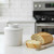 A Cafe Matte White Butter Bell Crock on a kitchen island with a buttered slice of a baguette