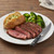 A Messermeister Avanta Damascus Steak Knife on a plate of sliced steak, baked potato and broccoli