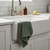 A Now Designs Ripple Elm Green Dish Towel draped over a kitchen sink