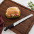 The Messermeister Pro Series Scalloped Baker's Knife on a cutting board with a ham and cheese sandwich on a ciabatta roll.