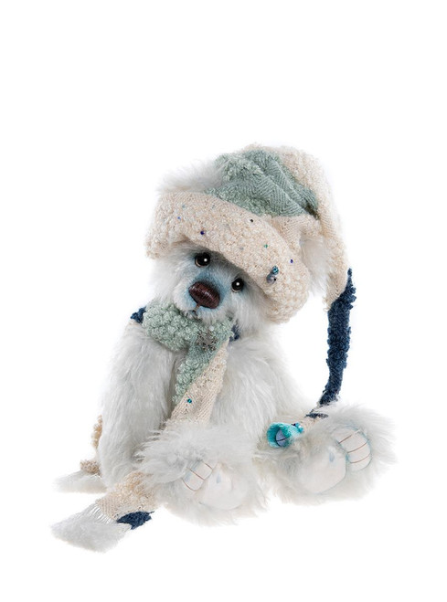 A white fluffy Charlie Bears teddy bear sits wearing a cream and sage knitted hat with a long tail, a matching scarf, and holding a small teal bell ornament.