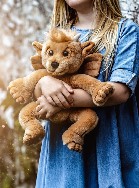 A tan/golden dragon-styled teddy bear sits upright, featuring wings, small horns, pointed ears, and large clawed feet, photographed against a white background.
