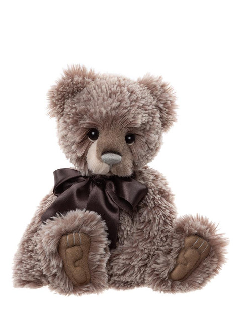 A plush teddy bear sits upright against a white background, featuring curly grey-brown fur, dark button eyes, suede paw pads, and a dark brown satin ribbon bow at its neck.